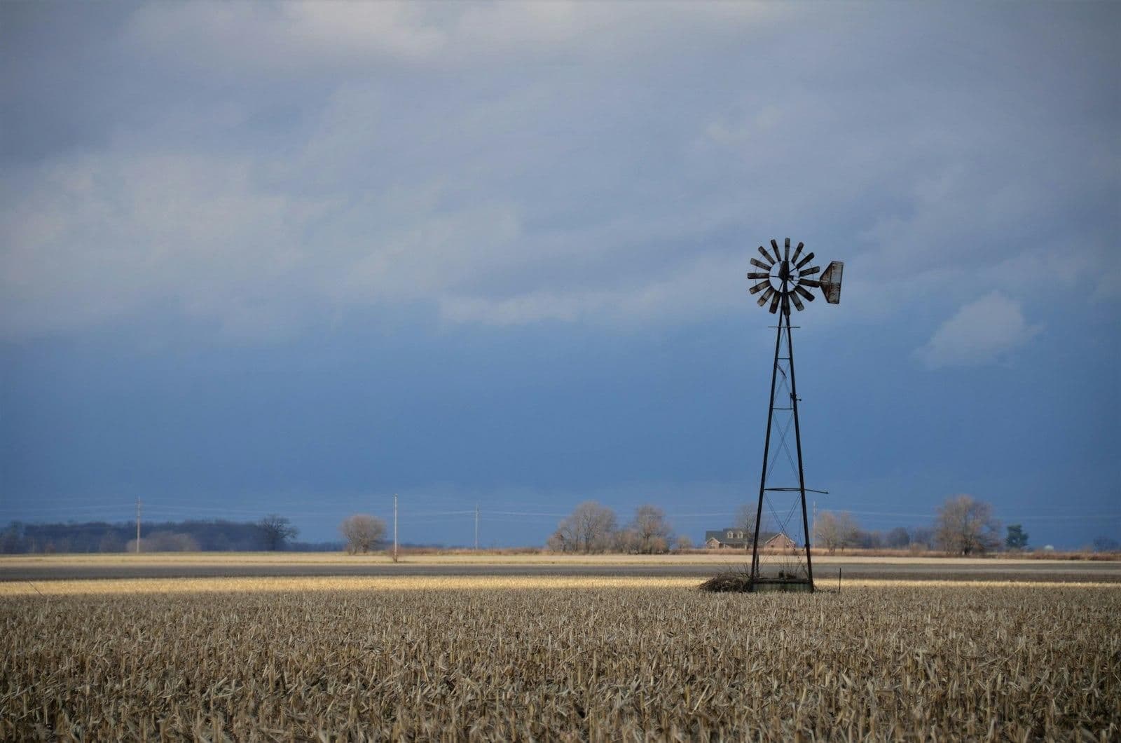 Traditional windmill standing in an open rural field beneath a cloudy blue sky