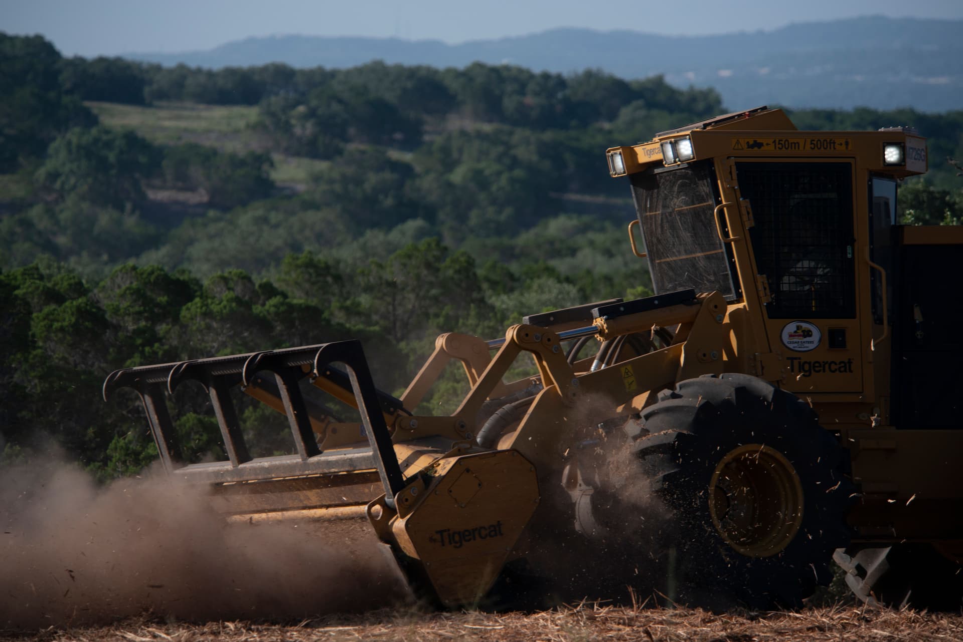 Yellow forestry mulcher working through brush on a hillside, with rolling Texas hills behind it