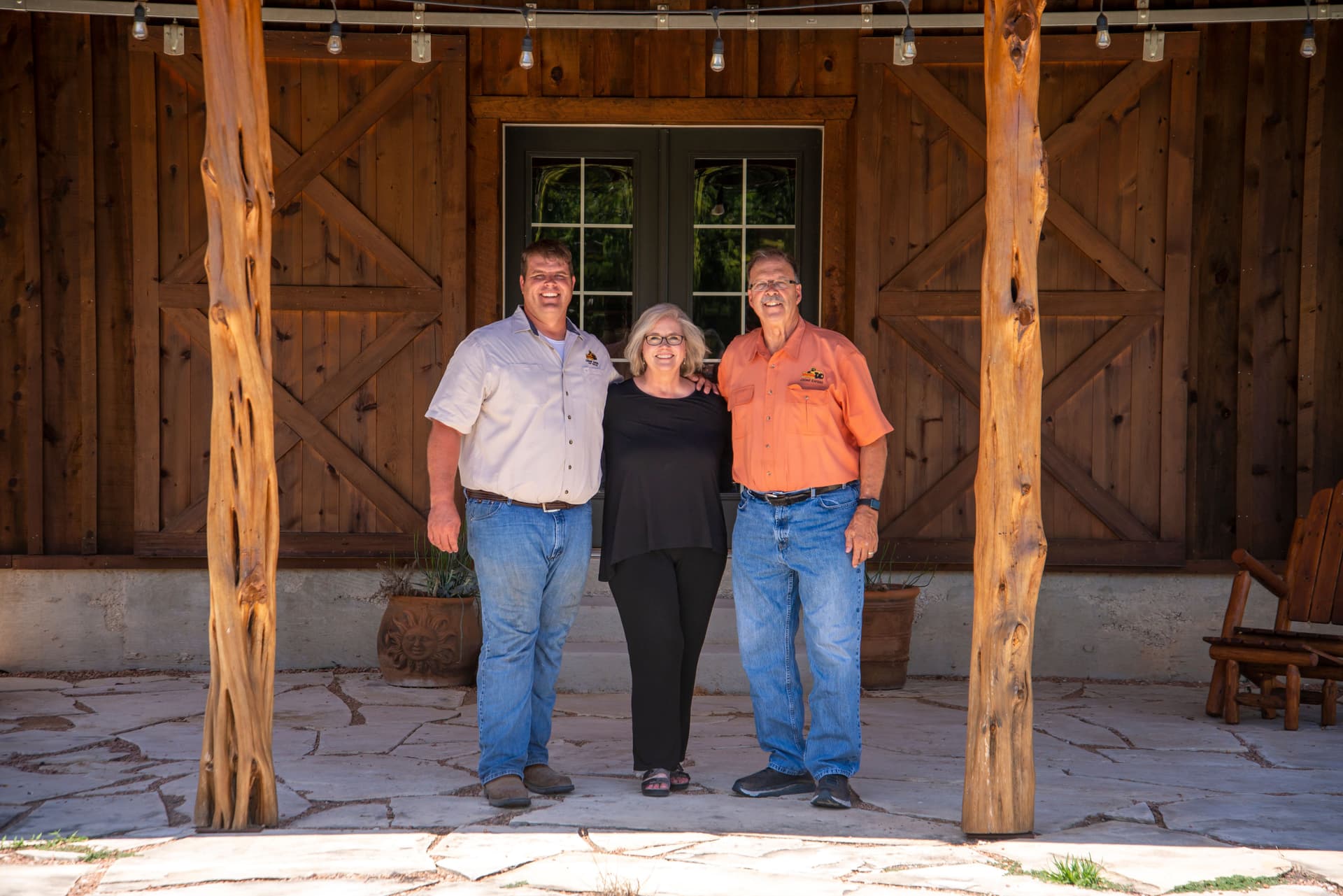 Two men and a woman standing on the porch of a ranch house with cedar log posts