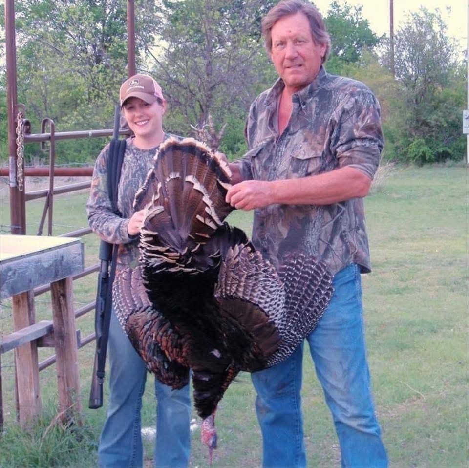 Young woman with a shotgun and her father holding a harvested wild turkey outdoors after a Texas turkey hunt