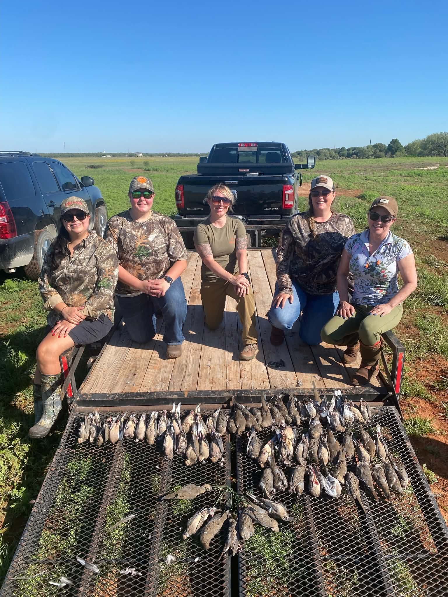  Five women hunters in camo seated on a trailer displaying a row of harvested dove after a Texas dove hunt