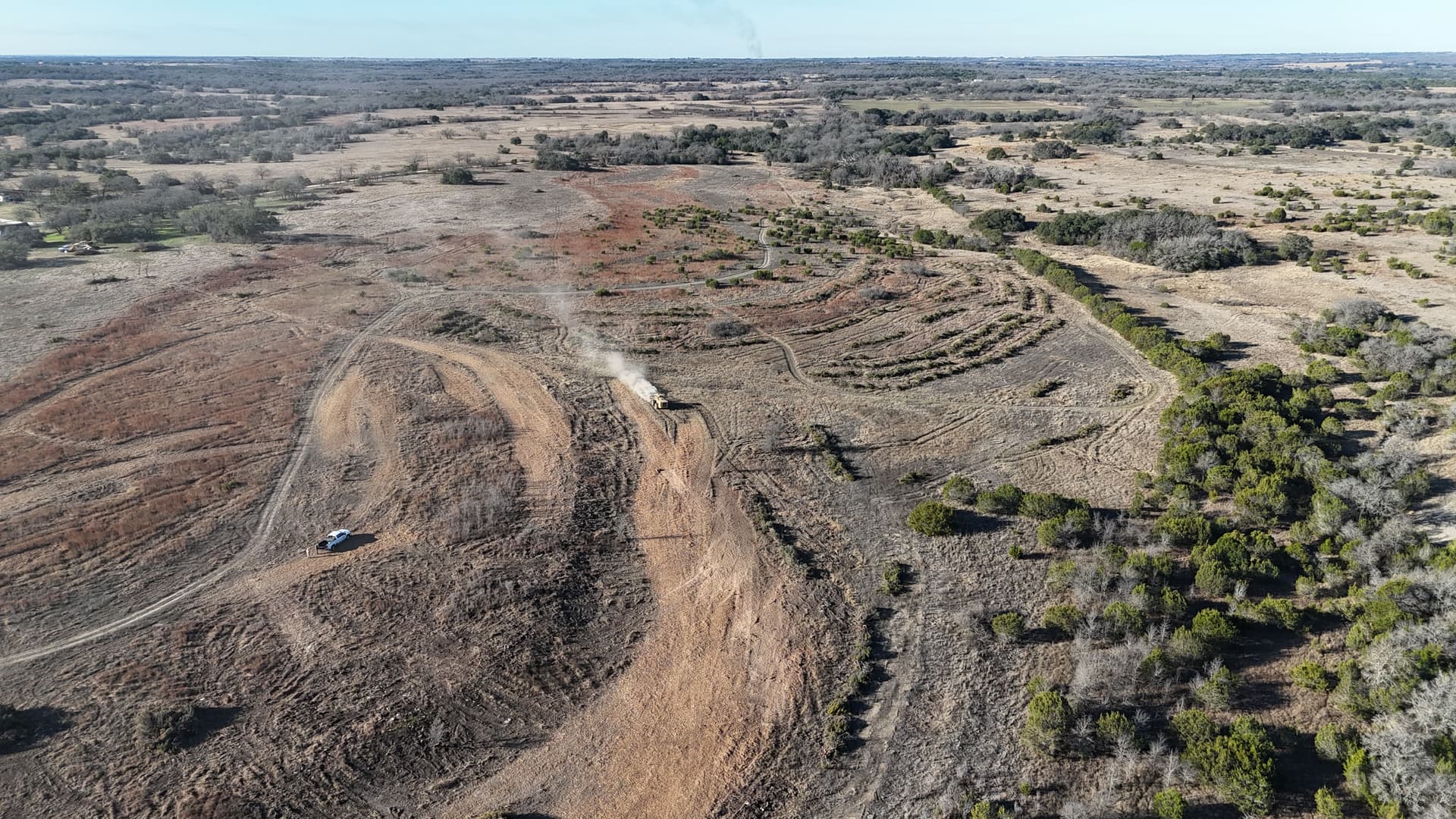 Aerial view of a hilltop mulched in curved lines that follow the land's natural contour, with a dirt road running through it