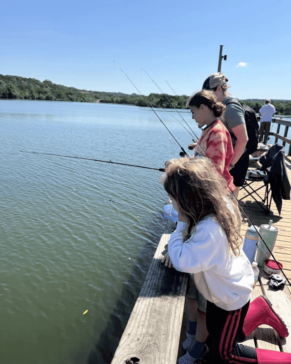 Women and a young girl fishing with rods from a wooden dock on a calm Texas lake on a sunny day