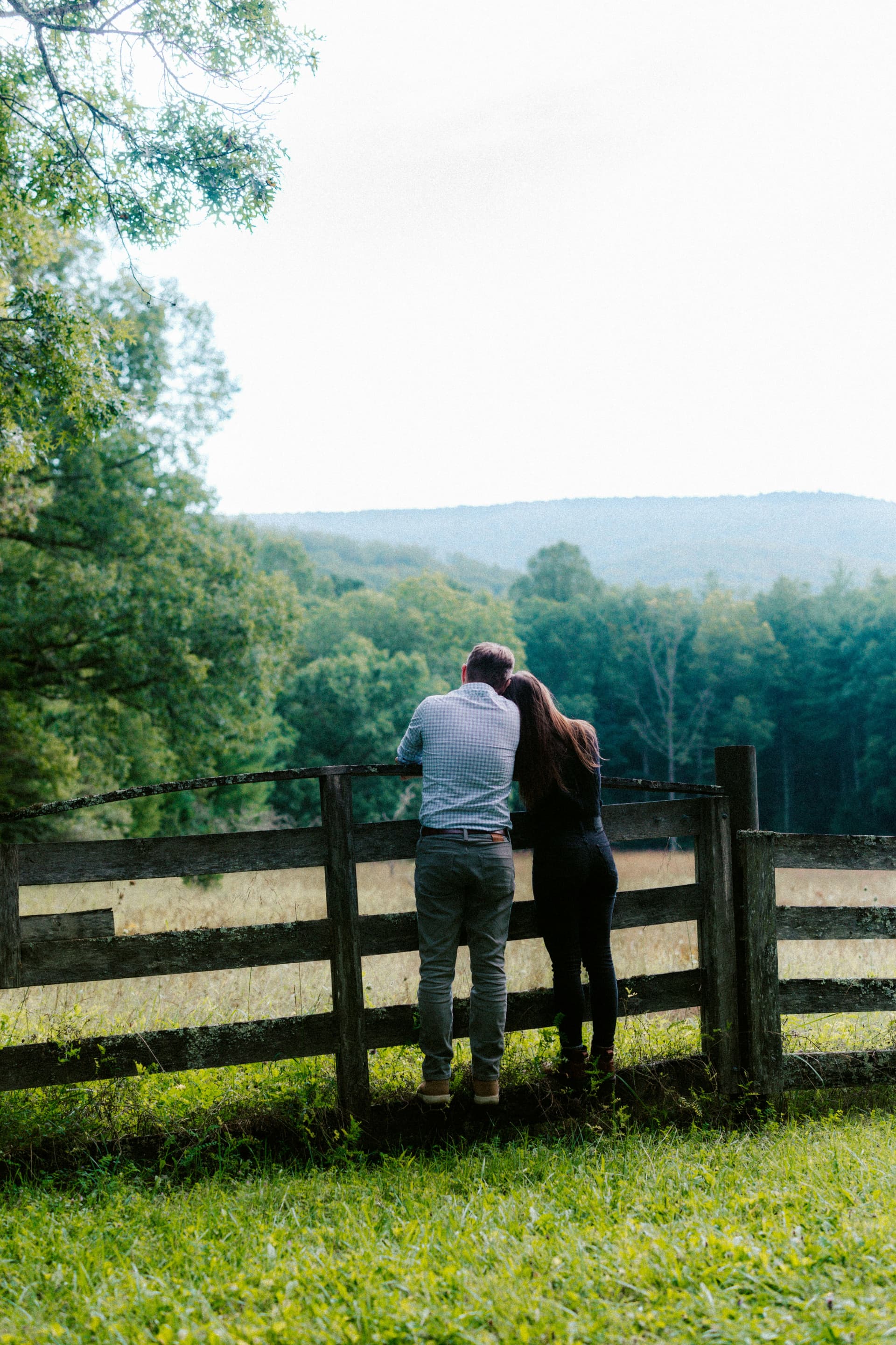 Couple at a wooden fence looking out over rolling green land they're considering buying